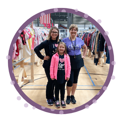 A mom and her three kids stand in front of a rack of girls clothes at their local BF sale.